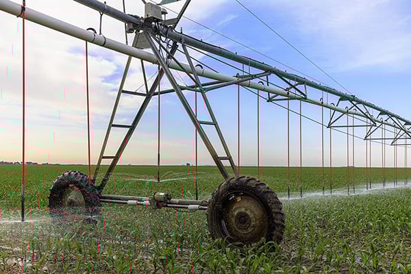 Center pivot irrigation system watering a green field under a blue sky.