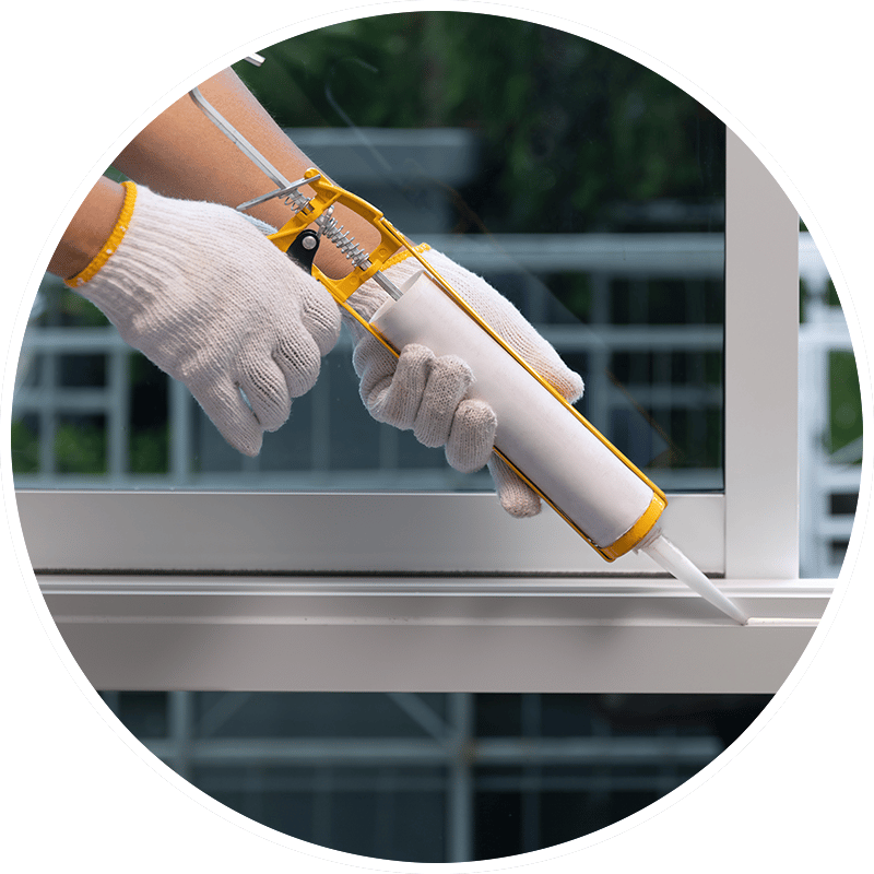 Person in gloves caulking a window frame with a caulk gun.