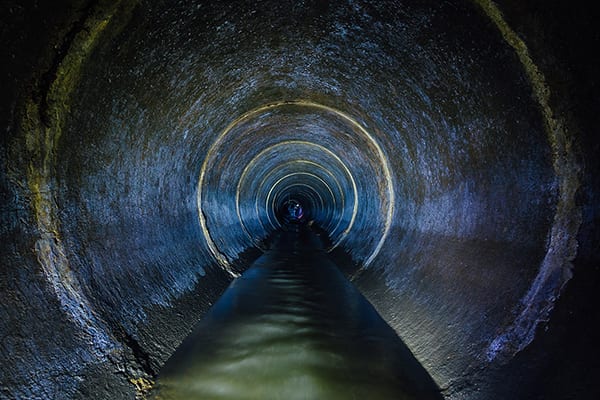 Dark underground sewer round concrete tunnel. Industrial wastewater and urban sewage flowing throw sewer pipe