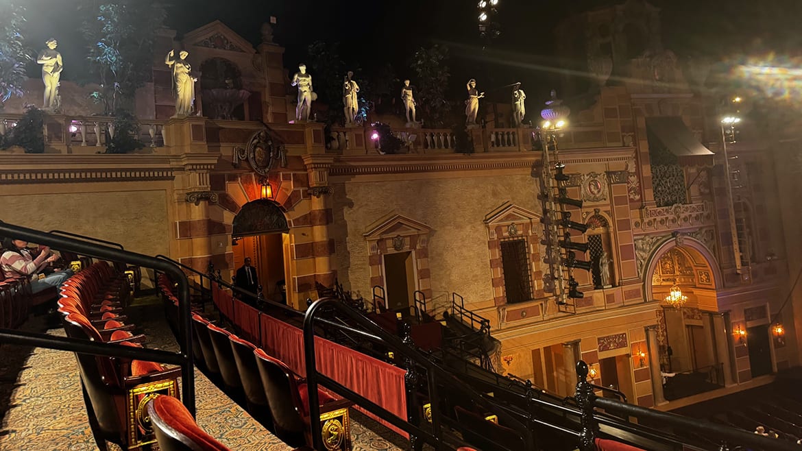 Ornate theater interior with balconies, classical statues, and rows of red velvet seats under dim lighting.