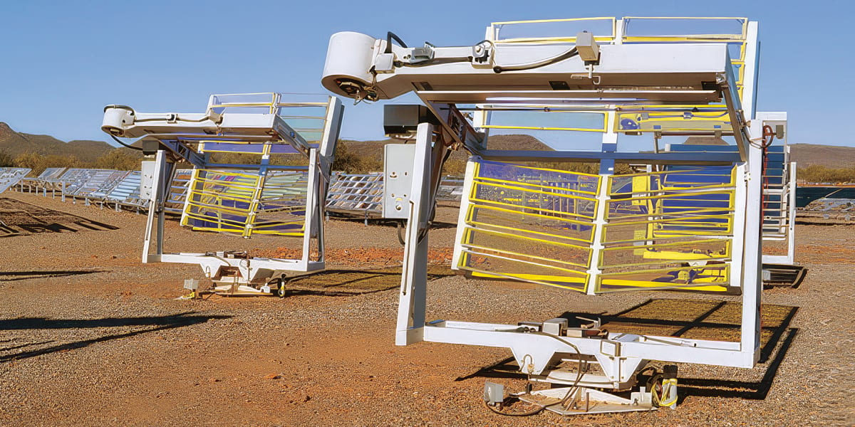 Two large solar thermal collectors with linear Fresnel mirrors in a sunny, arid landscape.