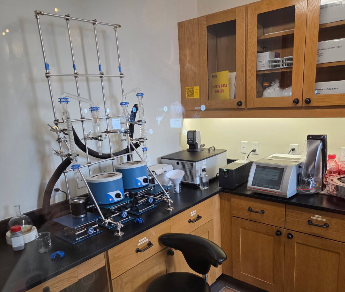 A lab bench with a complex distillation setup on the left and various electronic instruments on the right.