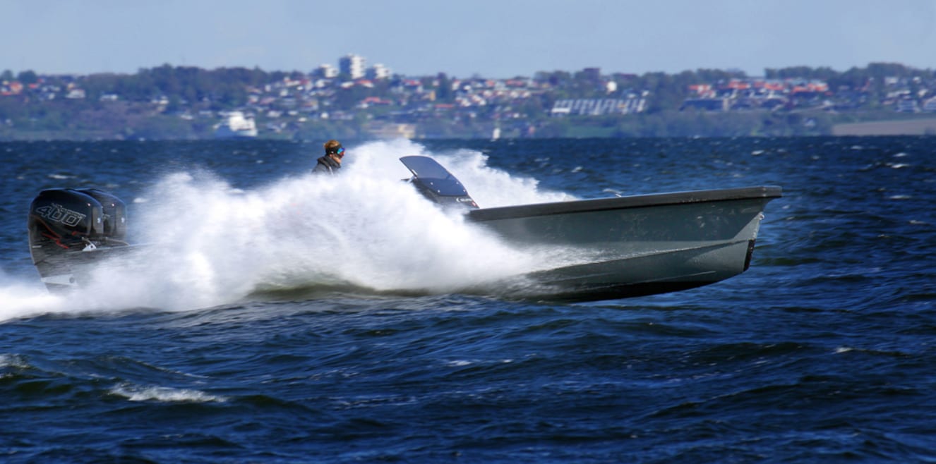 Speedboat with twin outboards kicks up spray on choppy water. Driver aboard.