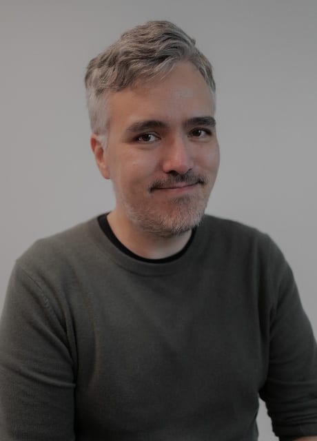 Smiling man with gray hair and beard in a dark sweater.