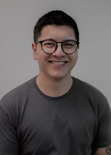 Smiling man with dark hair, glasses, and a dark grey t-shirt.