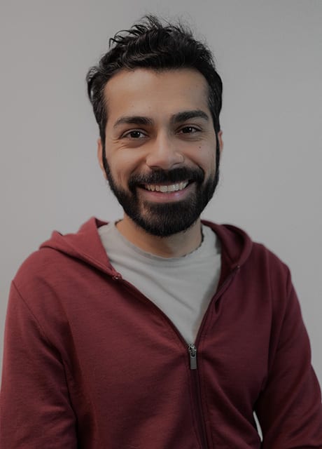 Smiling man with dark hair and beard in a red hoodie.