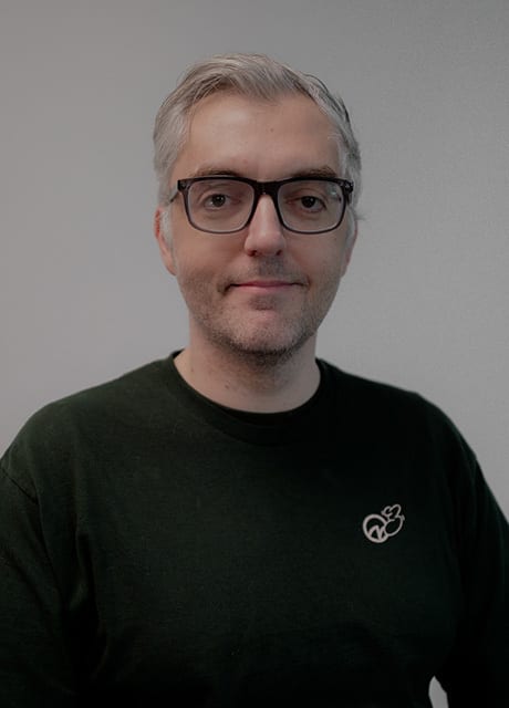 Gray-haired man with glasses in a dark green shirt with a white logo.