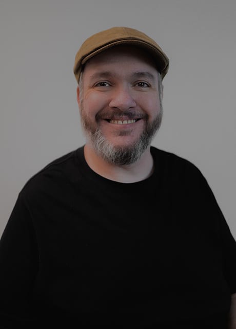 Smiling man in a brown flat cap and black t-shirt.