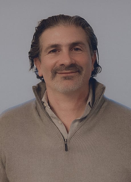 Headshot of a smiling man with dark, wavy hair and a beard, wearing a ribbed sweater.