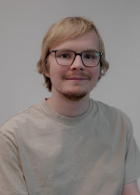 Blonde man with glasses smiles, wearing a light t-shirt.