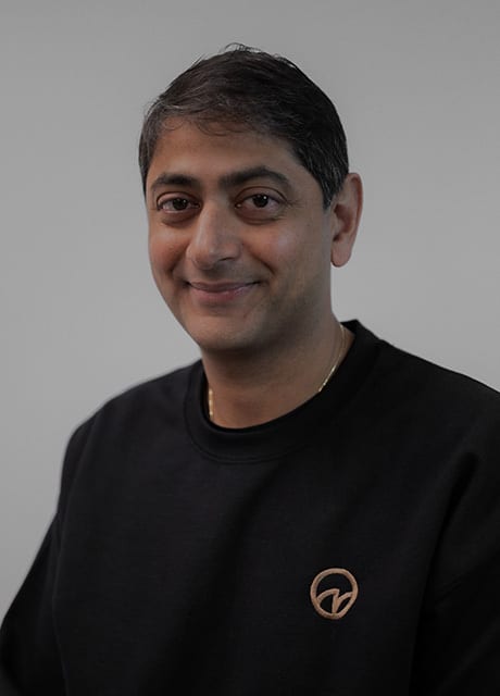 Smiling man in a black sweatshirt and gold chain.