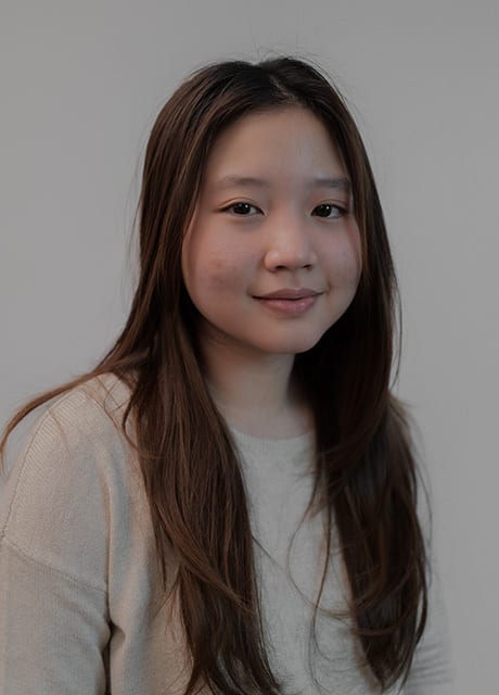 Smiling young East Asian woman with long brown hair, wearing a light sweater.