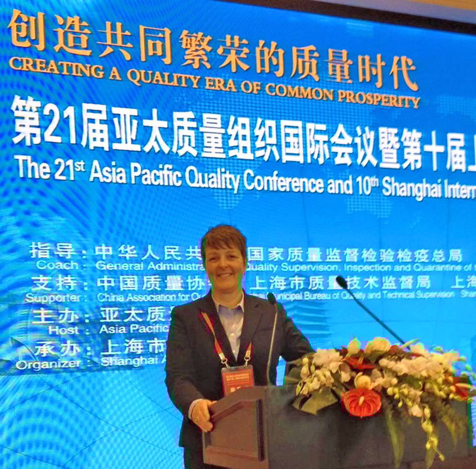 Woman smiling at a podium, with a blue conference banner displaying text in Chinese and English.