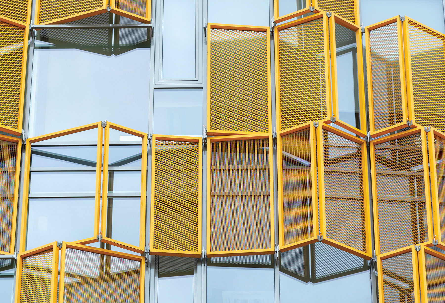 Modern building facade with vibrant yellow geometric perforated screens folded over glass.