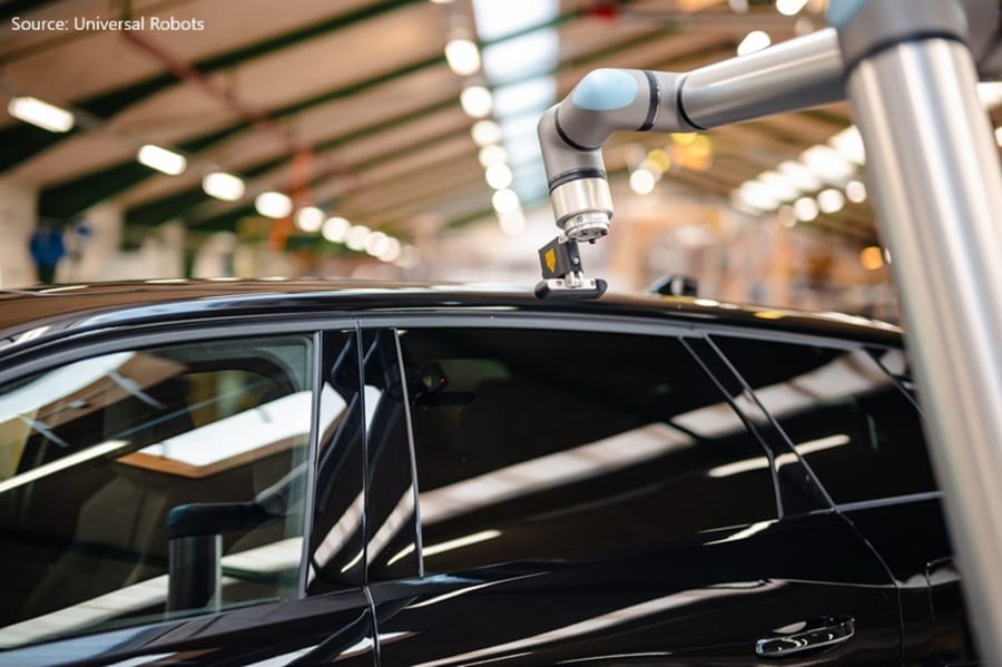 Robotic arm inspects a black car's roof in a factory setting.