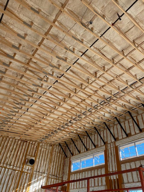 Insulated ceiling and walls of a building under construction with exposed wood framing and windows.