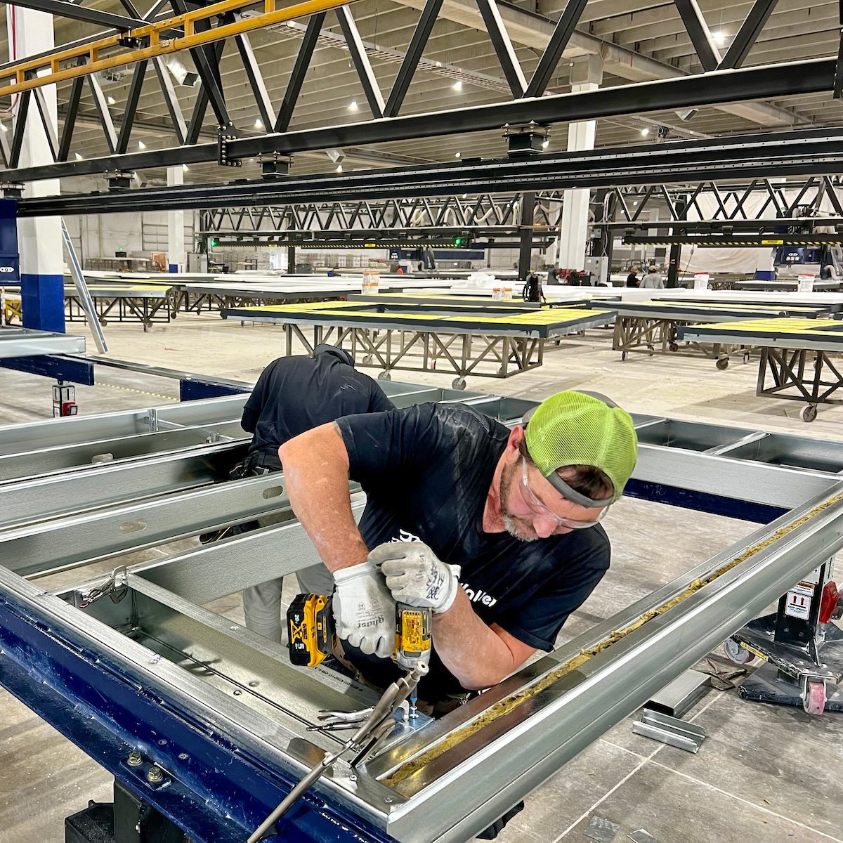 Worker using a power drill to assemble a metal frame in an industrial setting.