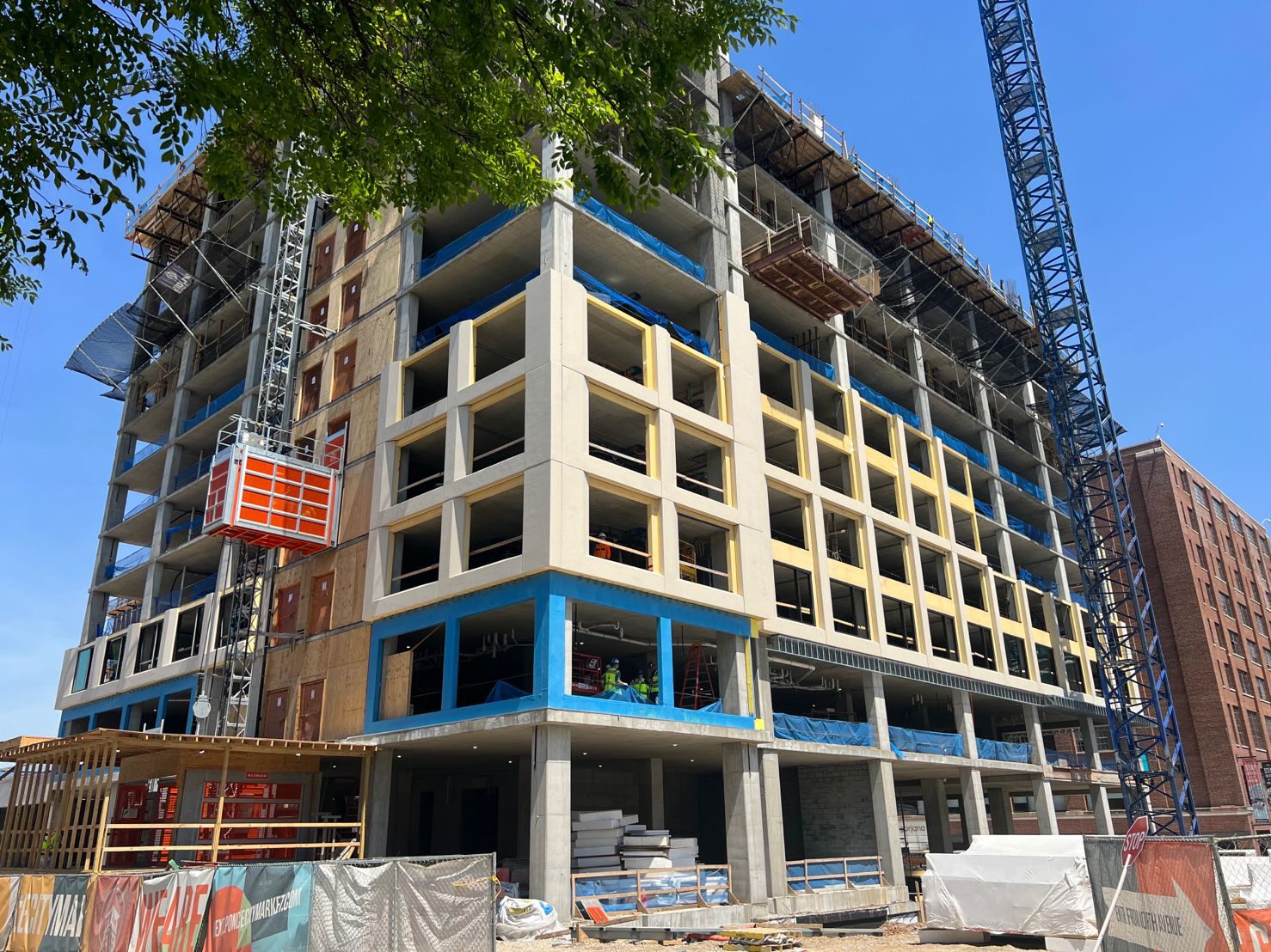 Multi-story concrete building under construction with an orange external lift and a blue crane.