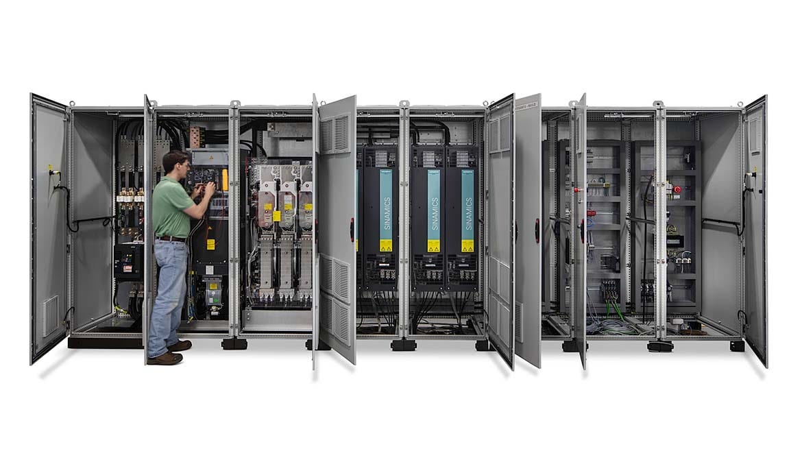 Man working on an open electrical cabinet among a row of industrial control panels.