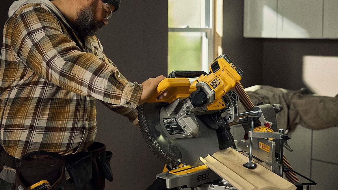 Man in plaid shirt cutting wood with a DeWalt miter saw.