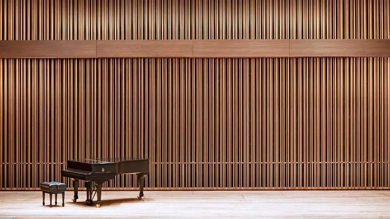 Grand piano and stool on a concert stage with a wall of vertical wooden slats.
