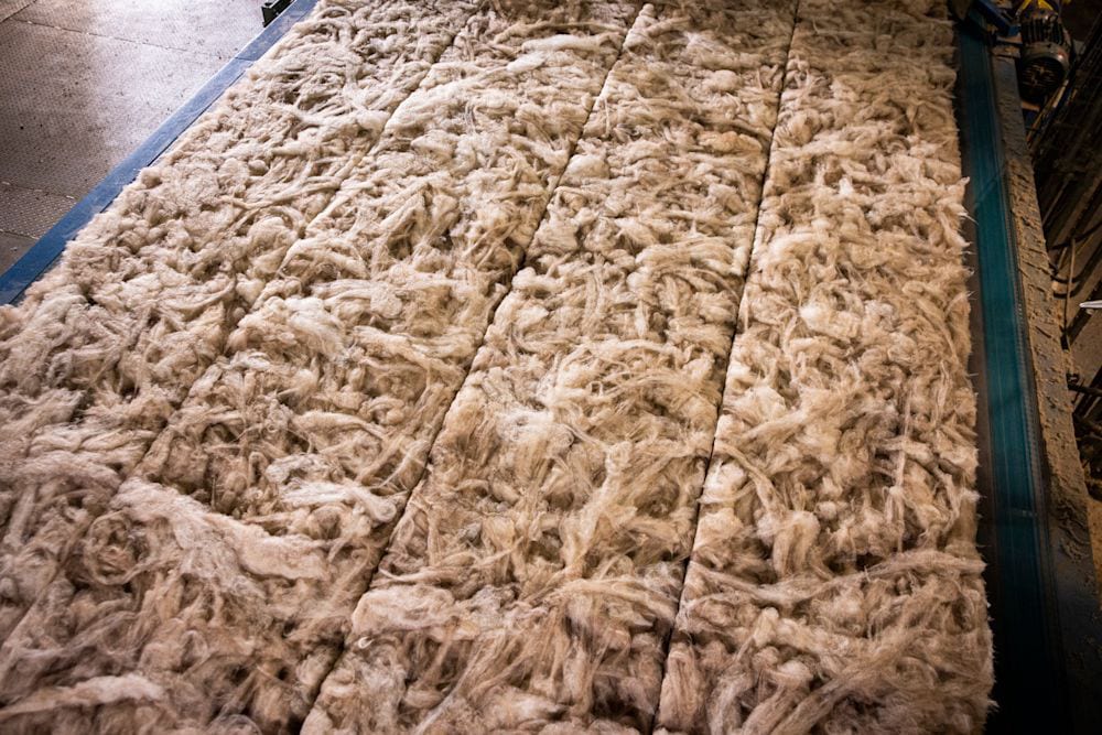 Close-up of light brown fibrous material, possibly wool or insulation, laid out in sections.