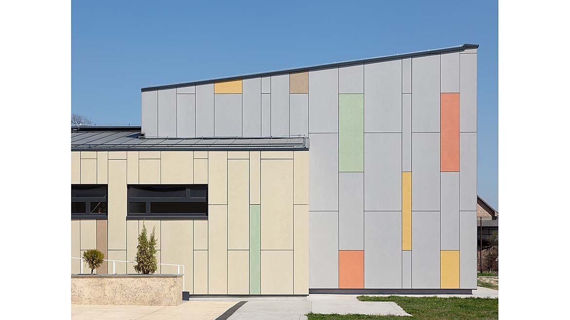 Modern building with cream and gray panels, colorful accents, and a slanted roof.