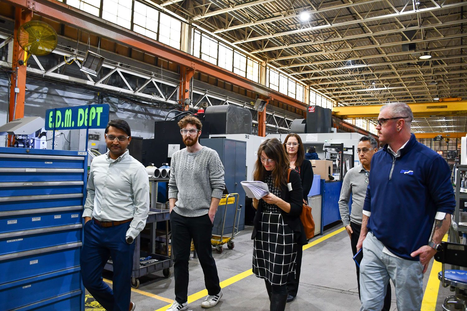 A group of six people, including three men and three women, walk through an industrial EDM department.