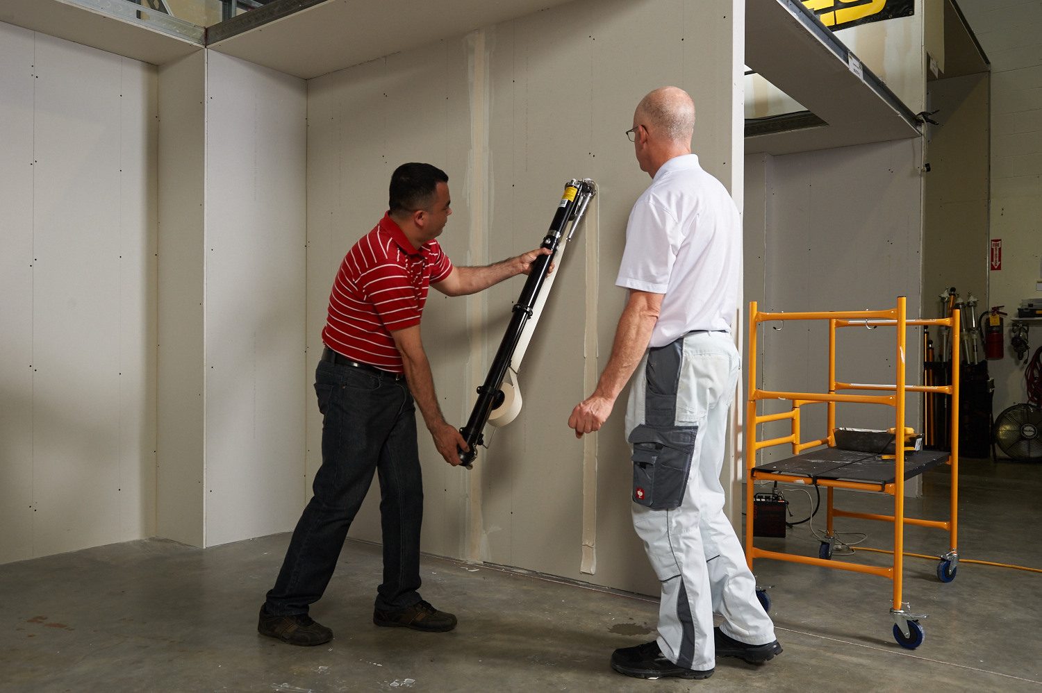 Two men applying drywall tape to seams using a taping tool.