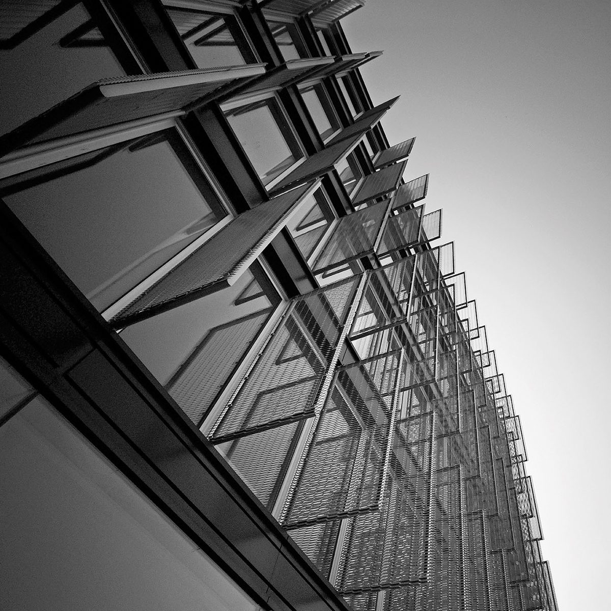 Black and white architectural photo of a modern building facade with angled, perforated sun shades.