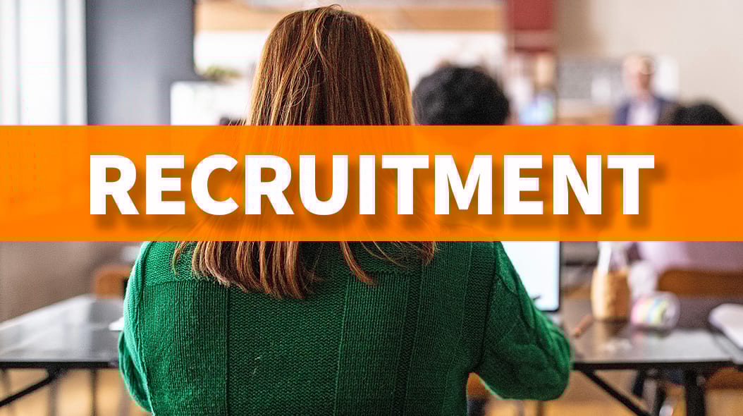 A person in a green sweater sits at a desk in an office, with 'RECRUITMENT' text overlaid.