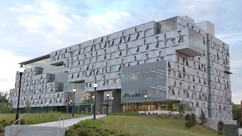 A modern building with a unique geometric facade, glass, and landscaped surroundings.