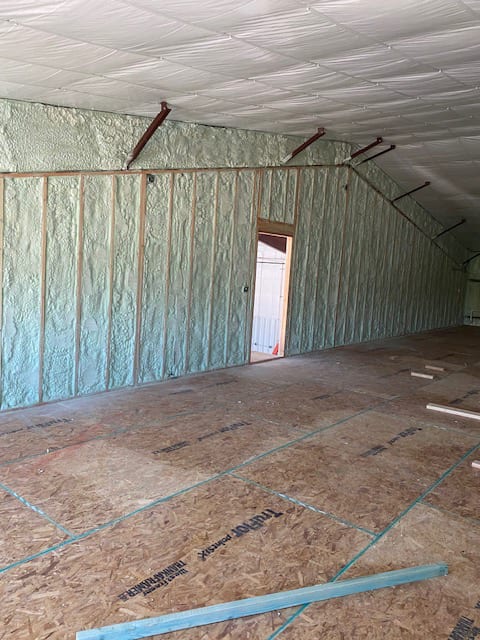 Room under construction with spray foam insulation on walls and ceiling, and OSB subfloor.