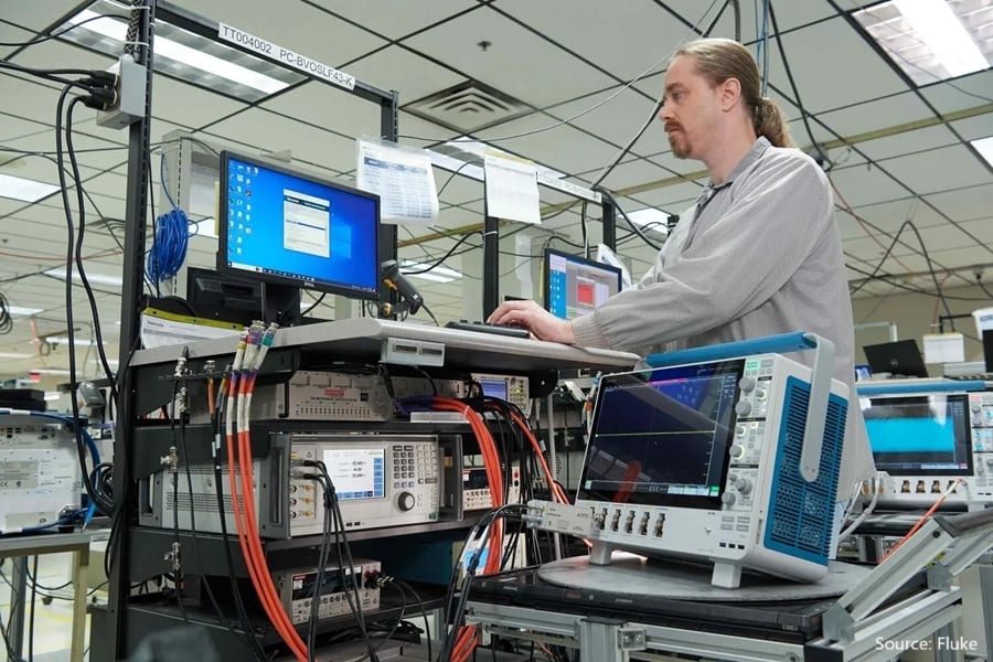 Man operates computers and electronic test equipment, including an oscilloscope, in a lab setting.