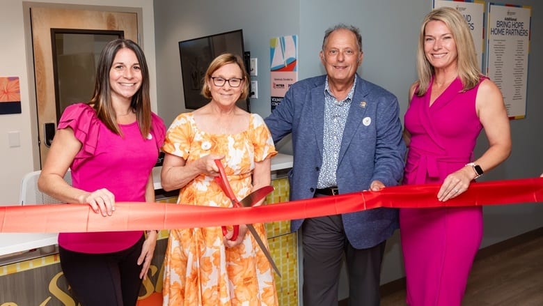 Four people, including a woman with scissors, ready to cut a red ribbon.