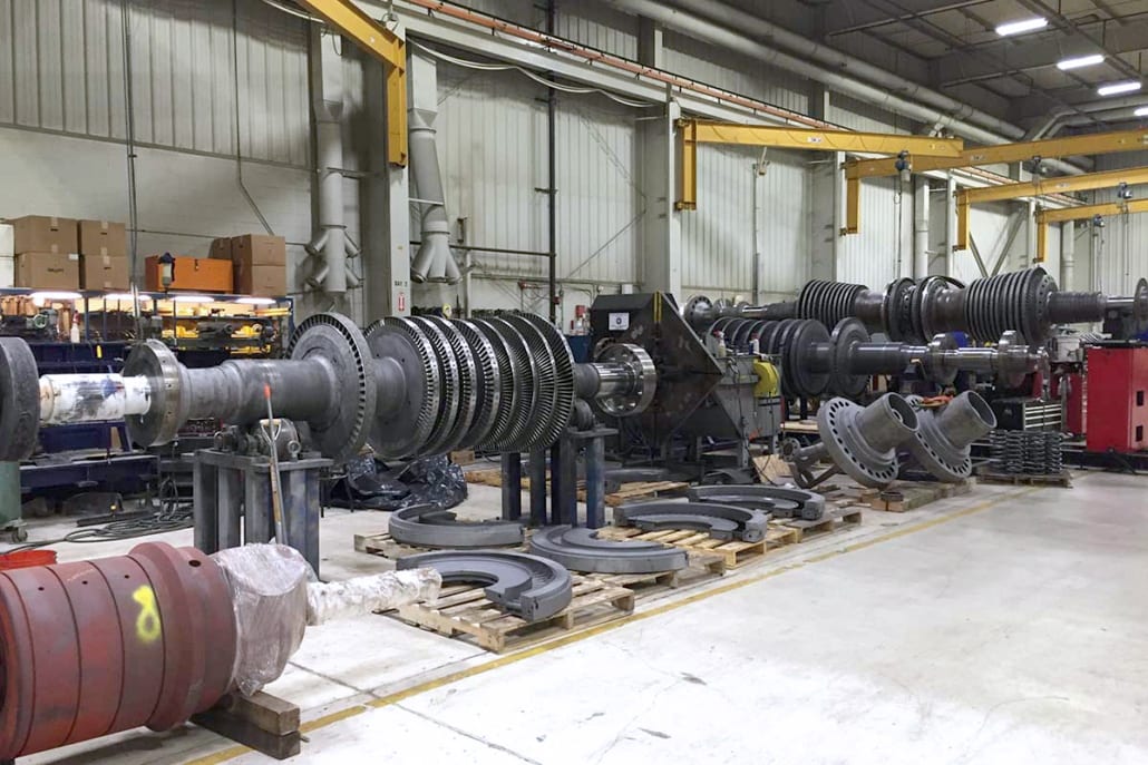Disassembled turbine components, including rotors and casings, laid out in an industrial workshop.