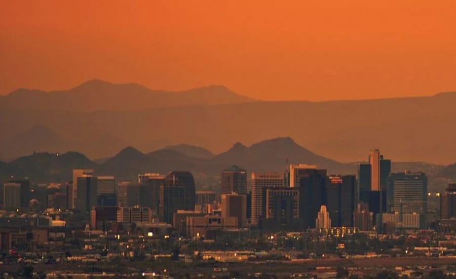 Orange sky over city skyline and mountains at dusk.