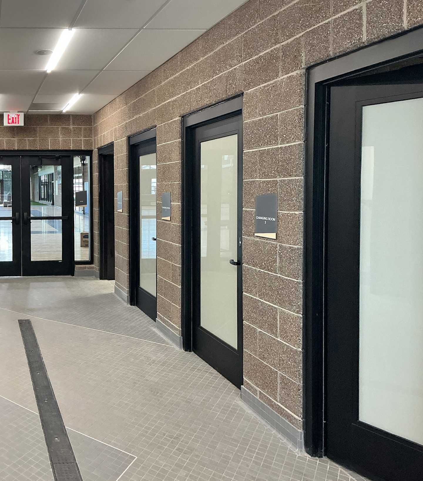 A modern hallway with multiple black-framed glass doors, labeled 'Changing Room', along a brick wall.
