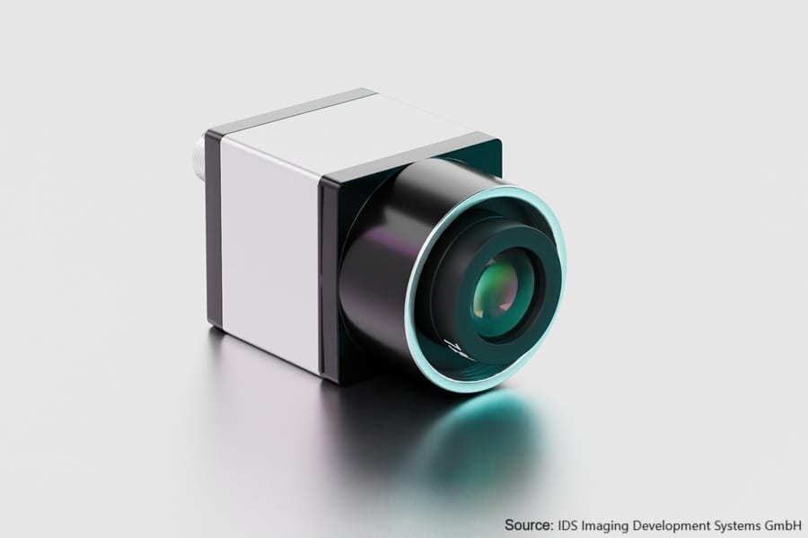 A white and black industrial camera with a lens on a reflective surface.