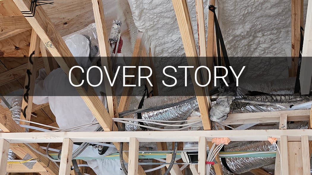 View of a residential attic under construction, showing wooden trusses, spray foam insulation, ductwork, and wiring.