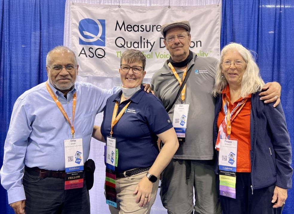 Four people smiling at an ASQ event, standing in front of a banner.