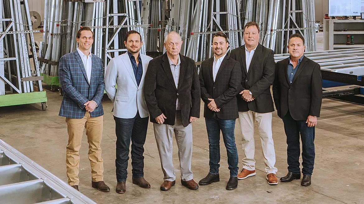 Six men in blazers posing in a warehouse.