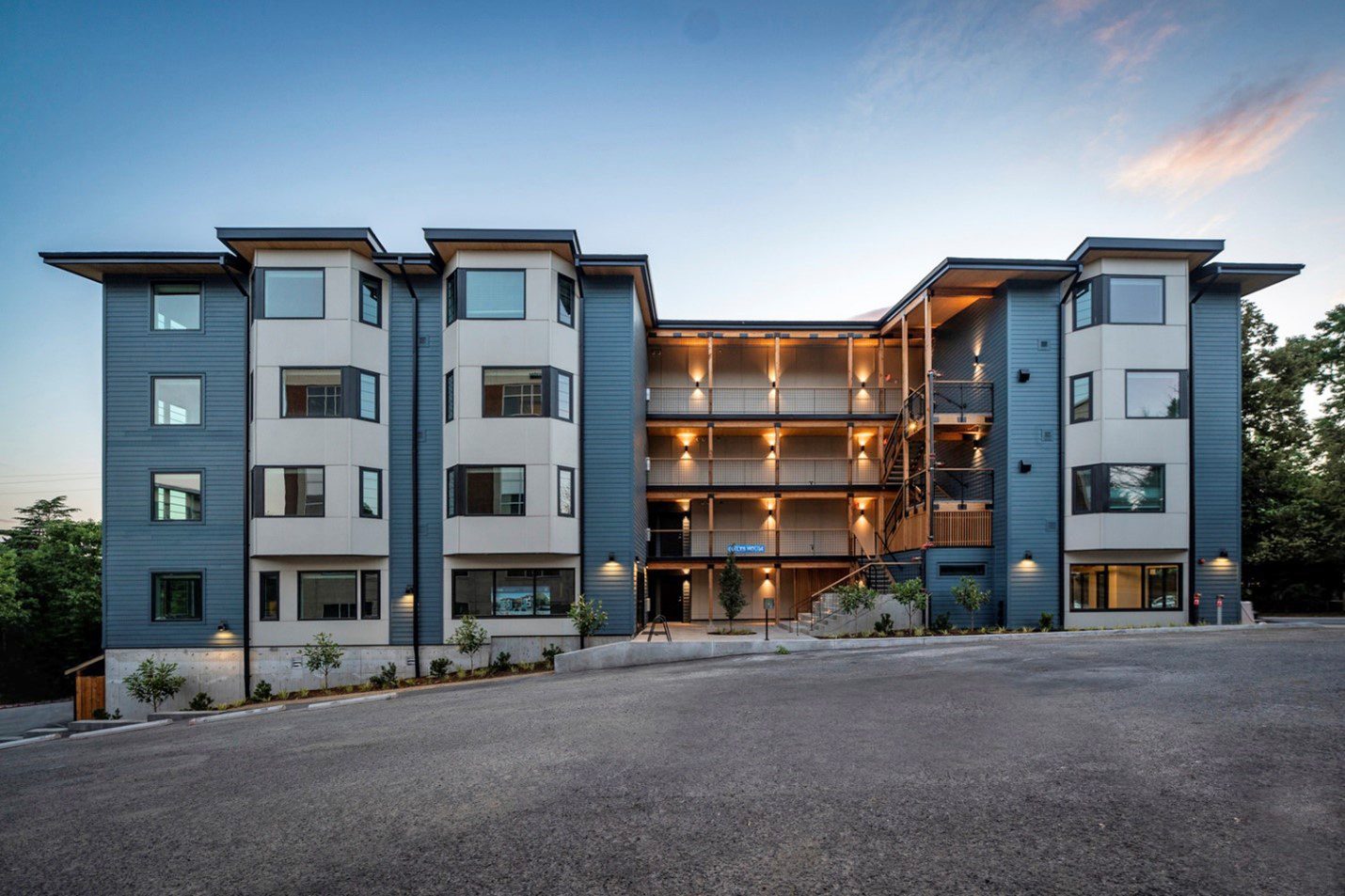 Modern blue and white apartment building with an illuminated open central courtyard at dusk.