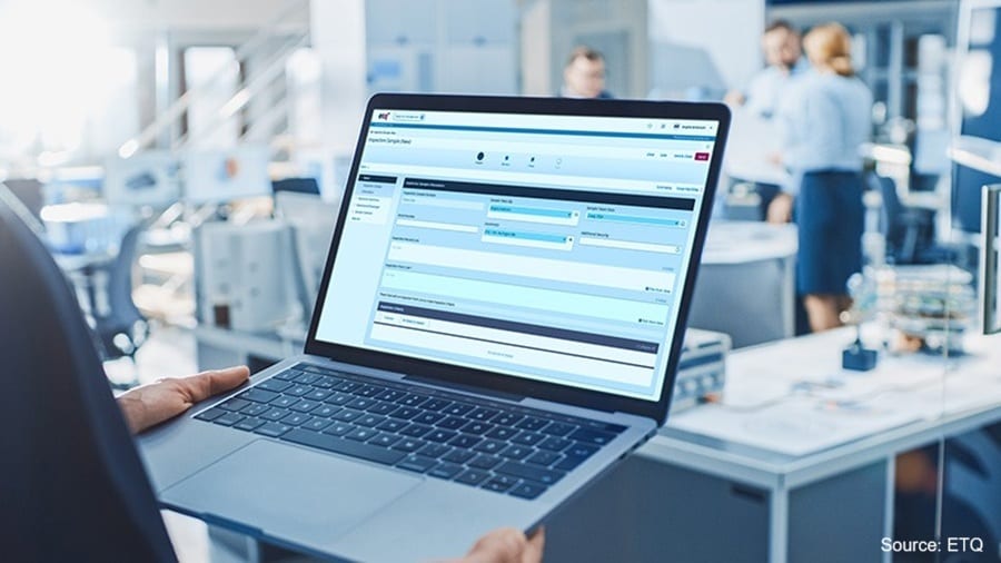 Person holding laptop with business software, blurred office background with colleagues.