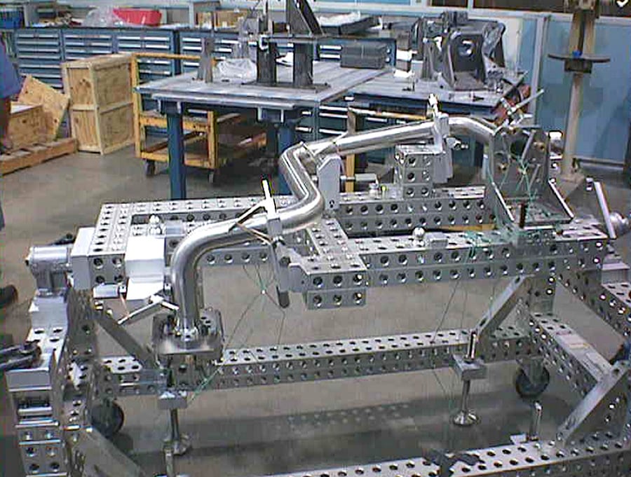 Modular fixturing system holding a bent metal pipe in a workshop.