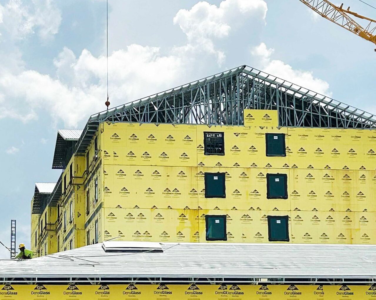 Building under construction with yellow DensGlass sheathing and metal roof trusses, under a cloudy sky.