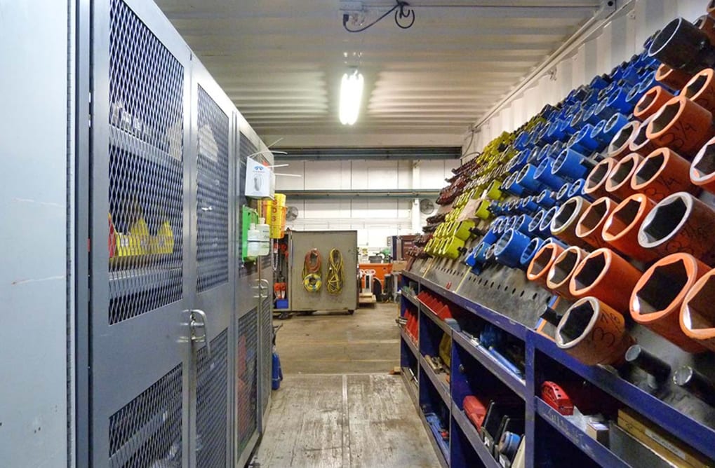 Workshop aisle with metal grated storage cabinets and racks of colorful tools.