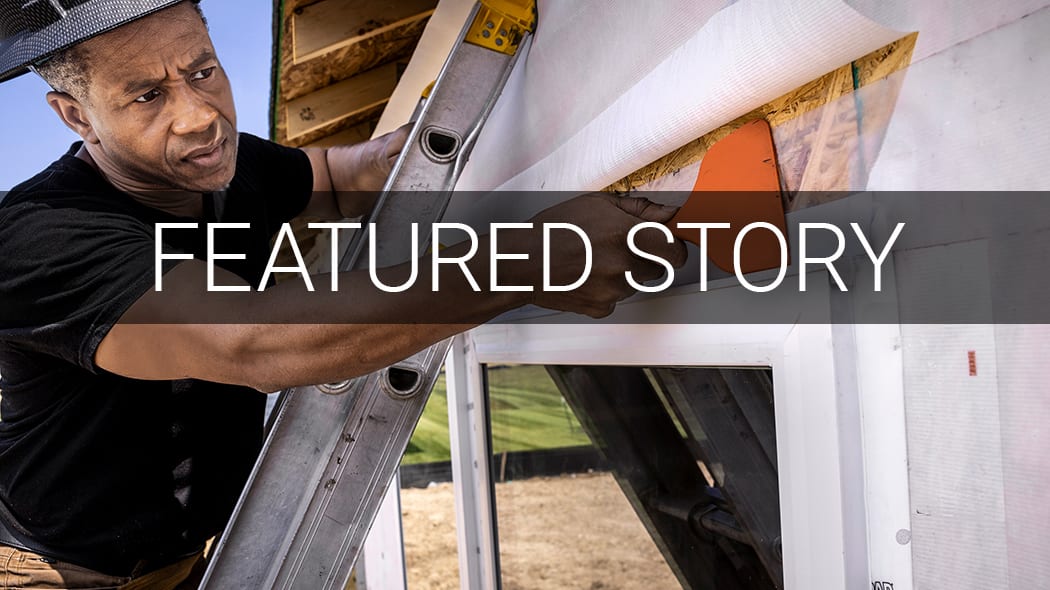 Man on a ladder installing house wrap on the exterior of a building.