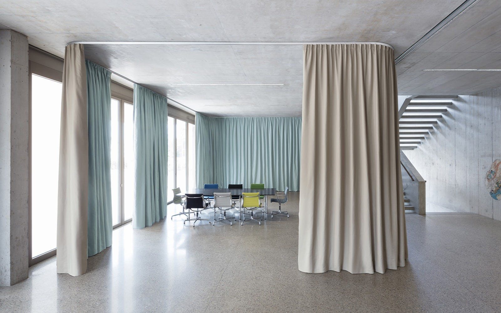 Modern conference room with colorful chairs, concrete walls, and flowing beige and light blue curtains.