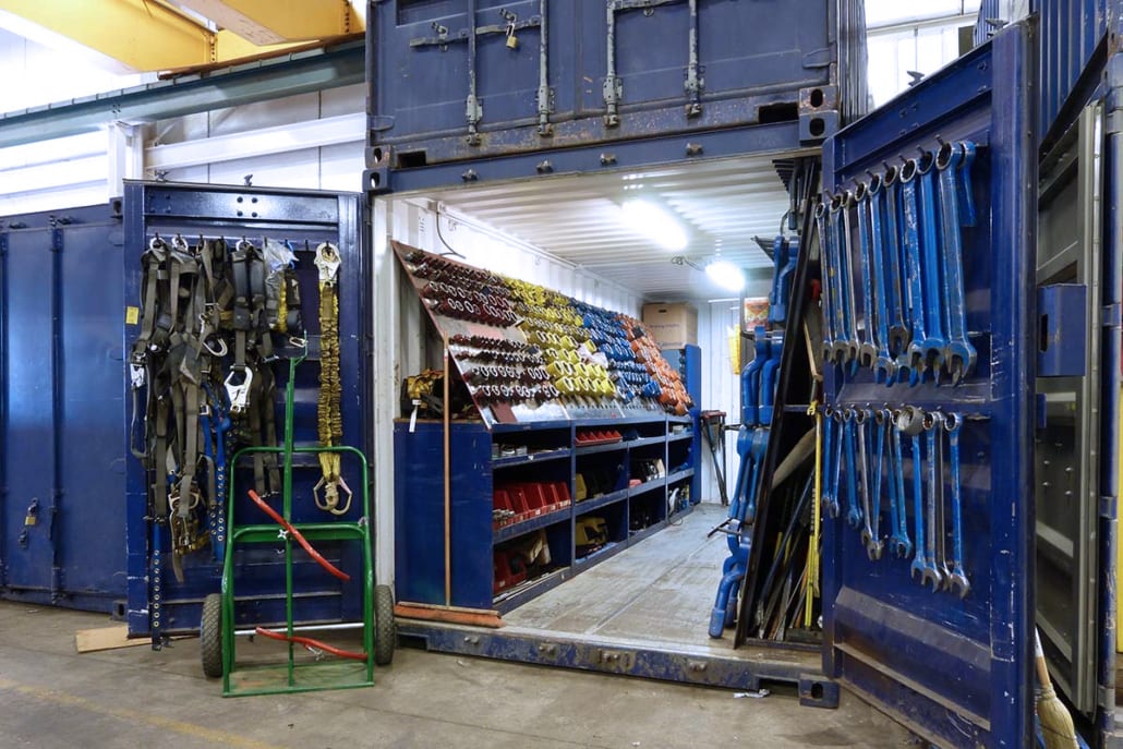 Open shipping container converted into a tool workshop with organized harnesses, wrenches, and equipment.